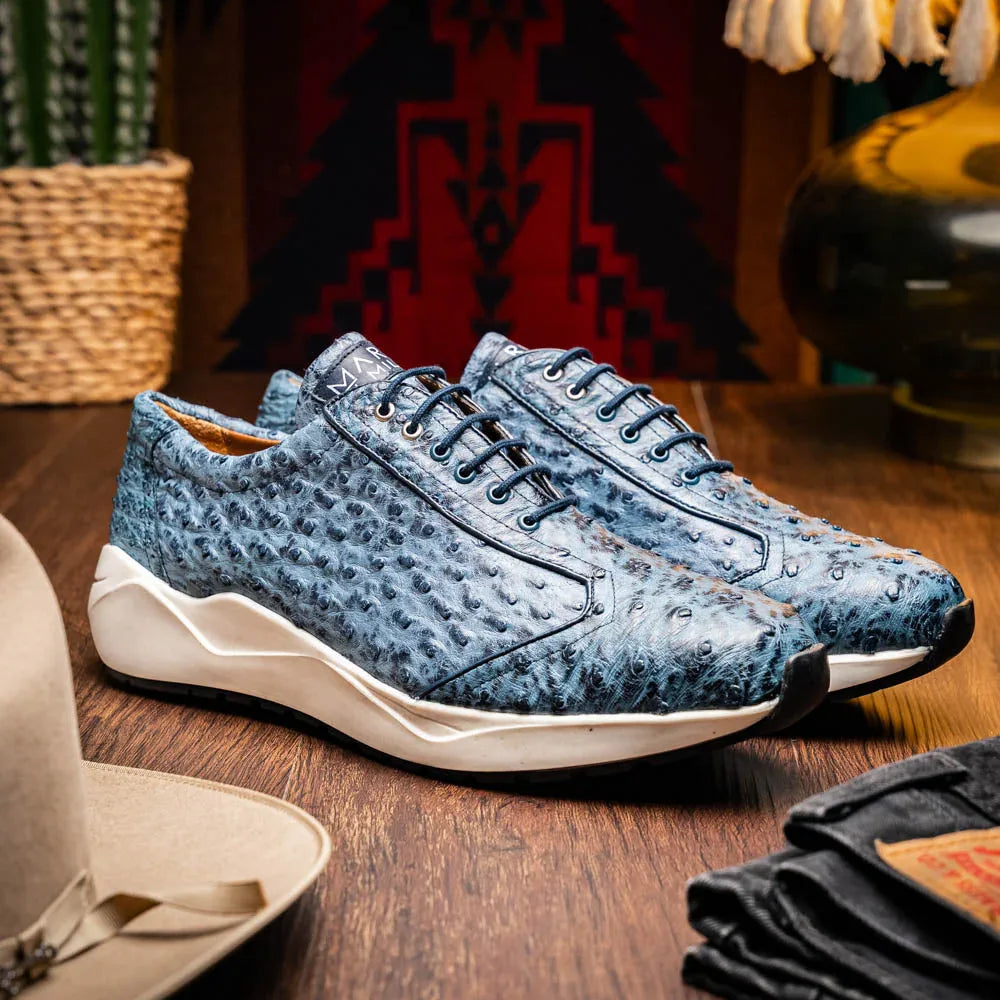 Model walking outdoors wearing navy blue ostrich skin sneakers paired with casual pants.