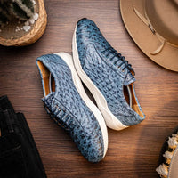 Close-up of navy blue ostrich leather sneaker laced up, resting on concrete surface in city environment.