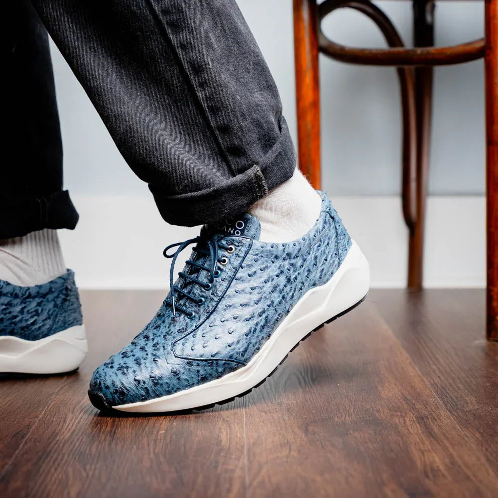 Model walking showing off navy blue ostrich leather sneakers with white anti-slip sole outdoors.