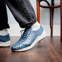 Model walking showing off navy blue ostrich leather sneakers with white anti-slip sole outdoors.
